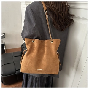 Detail of a brown suede tote bag with golden chain strap and FASHION logo on a model