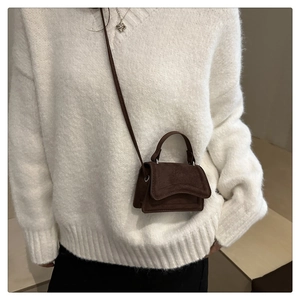 Détail d'un mini sac bandoulière en daim marron foncé porté avec un pull en tricot blanc