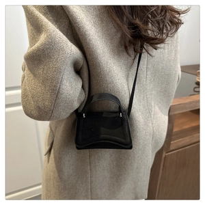 Détail du mini sac à main en daim noir avec base incurvée sur un manteau gris chic