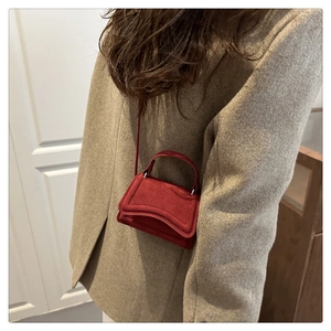 Détail du mini sac carré en daim bordeaux porté avec un manteau en laine kaki en intérieur