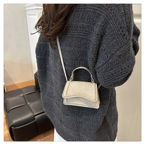 Détail d'un mini sac à bandoulière en daim beige porté sur un pull en maille grise