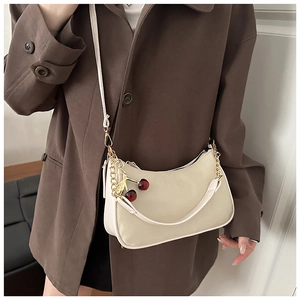 Détail d'un sac demi-lune crème avec breloque cerise rouge et bandoulière en cuir souple