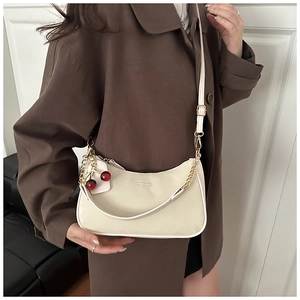 Detail of cream half-moon bag with cherry charm and chain strap worn on brown coat
