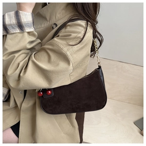 Detail of dark brown suede shoulder bag with gold chain strap and red cherry charm