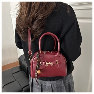 Detail of burgundy crossbody bag with gold buckle hardware and braided charm accessory
