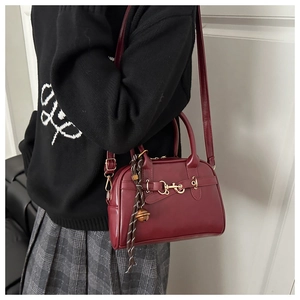Close-up of vintage dark red shell bag with gold horsebit buckle and woven charm strap