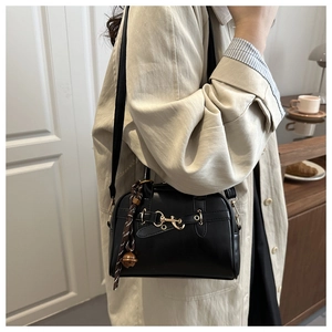 Detail of a vintage black leather crossbody bag with a gold horsebit buckle and charms