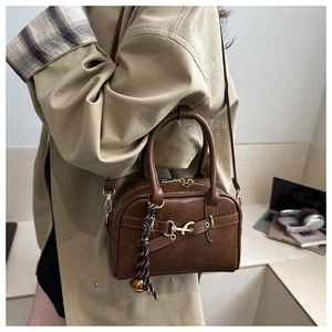 Detail of dark brown crossbody bag with gold hook buckle and woven ball charm accent