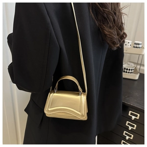 Detail of a chic gold metallic mini handbag featuring a unique wavy base on a black blazer