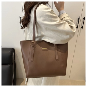 Detail of a brown leather tote bag featuring a metal brand plate and adjustable strap