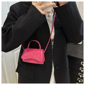 Gros plan d'un mini sac à main en cuir verni rose porté sur un blazer noir chic