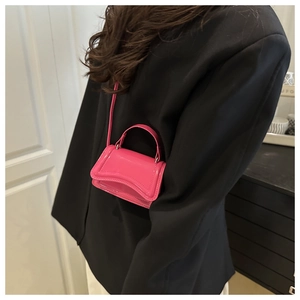 Detail of vibrant hot pink micro bag with wave-shaped flap and matching shoulder strap