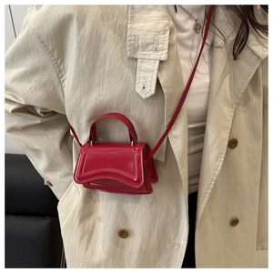 Détail du mini sac sablier en cuir verni rouge porté avec un trench-coat classique beige
