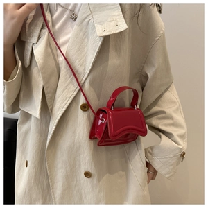 Close-up of red patent leather mini handbag with curved flap on a beige trench coat