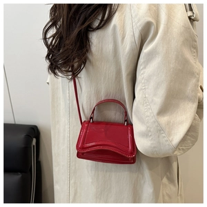 Detail of red patent leather mini handbag with wavy base worn with a beige trench coat