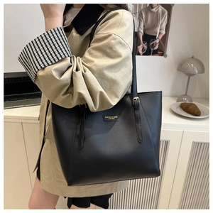 Detail of minimalist black faux leather tote bag with gold logo on beige background