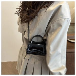 Détail d'un mini sac en cuir verni noir avec rabat ondulé et bandoulière réglable