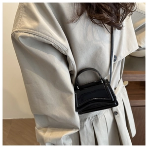 Détail d'un mini sac à main en cuir verni noir porté avec un trench-coat beige