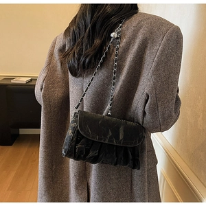 Close-up of black pleated texture shoulder bag with silver chain strap on wool coat