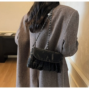 Detail of black pleated leather crossbody bag with chain strap on a grey suit model