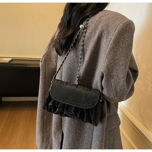Detail of black pleated cloud bag with silver chain strap on model's shoulder