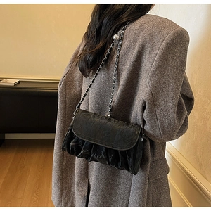 Detail of black pleated cloud bag with silver chain strap on a model shoulder