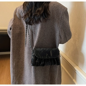 Detail of black pleated cloud bag with metallic chain strap on a brown blazer coat
