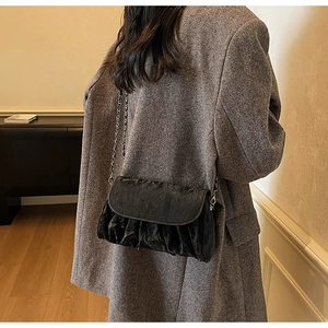 Detail of a black pleated cloud bag with silver chain worn over a grey wool coat