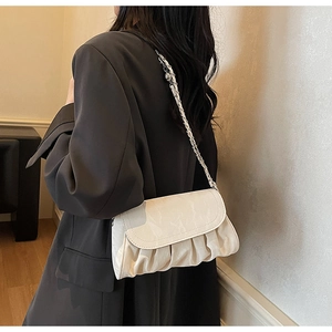 Detail of cream pleated cloud bag with silver chain strap on a dark blazer suit