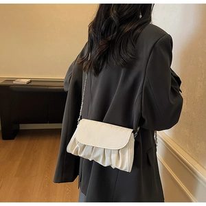 Detailed view of off-white pleated cloud bag with elegant metal chain strap on model