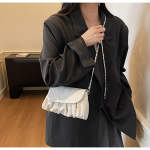 Close-up of ivory pleated cloud bag with silver chain strap on black blazer model