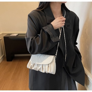 Close-up of pleated ivory crossbody bag with silver chain strap on black blazer