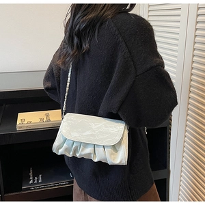 Detail of white pleated cloud bag with silver chain strap worn by a model