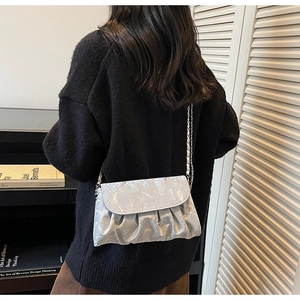 Detail of silver pleated cloud bag with metallic chain strap worn on black sweater