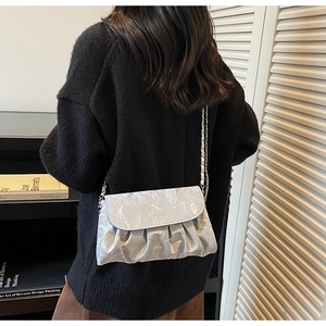 Detail of light blue pleated shoulder bag with metallic chain strap worn by a model
