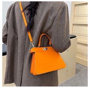 Detalle de bolso naranja con grabado de cocodrilo combinado con una chaqueta gris