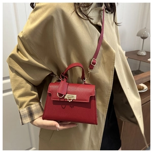 Dettaglio borsa Kelly in pelle rossa con chiusura dorata abbinata a un trench beige