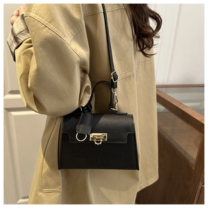 Detail view of a black pebble leather handbag with gold metal lock worn by a model