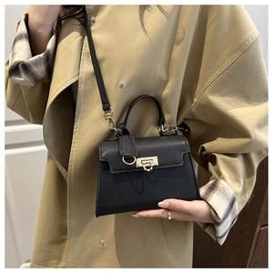 Detail of black lychee grain leather handbag with gold metal lock on khaki trench coat