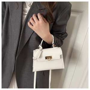 Detail view of a white pebble grain handbag with gold clasp and elegant metal top handle