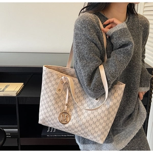 Detailed close-up of a beige tote bag featuring repeating M prints and a round metal charm