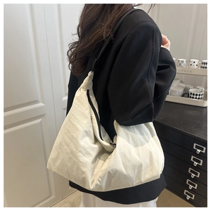 Detail of a large off-white tote bag with a wide black strap worn by a model