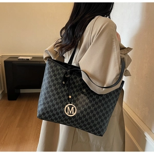 Detail of black tote bag with M-letter jacquard pattern and golden circular charm