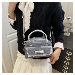Close-up of blue denim Boston bag with lace trim, silver bow, and checkered ribbon detail