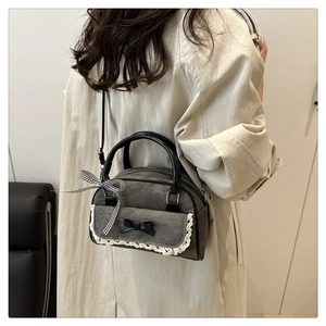 Close-up of grey bow Boston bag with lace trim worn over a beige trench coat