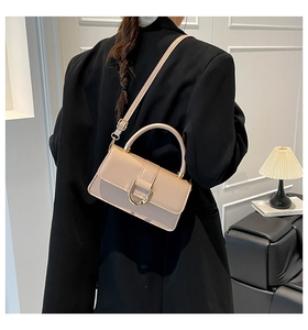 Detail of elegant beige square handbag with golden U-shaped clasp worn with black blazer