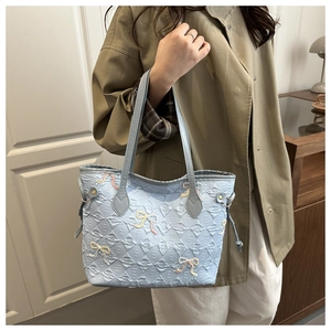 Detail of light blue tote bag with colorful embroidered bows and embossed E-pattern texture