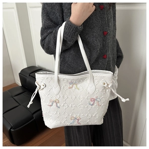 Detail of white quilted tote bag with colorful bow embroidery and side drawstrings