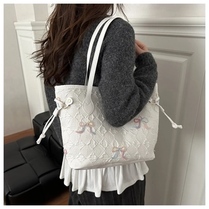 Detail of white quilted tote bag with colorful beaded bow and shoulder strap on model