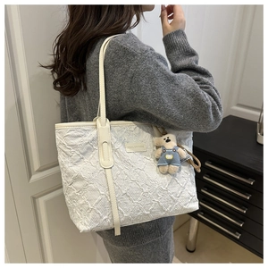 Gros plan du sac fourre-tout blanc avec texture florale en relief et pendentif ours